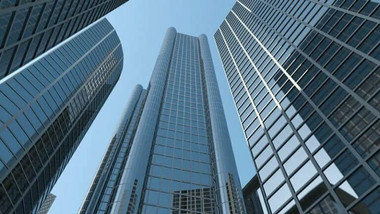 Tall, modern glass skyscrapers viewed from below against a clear blue sky, reflecting light on their sleek surfaces.