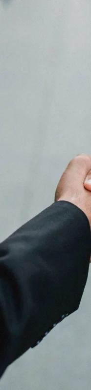 Two people in business attire are shaking hands on a city sidewalk, with only their arms and partial torsos visible.