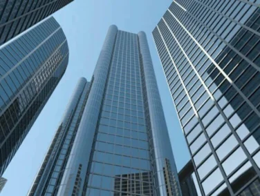 Tall modern skyscrapers with glass facades are shown from a low angle against a clear blue sky.