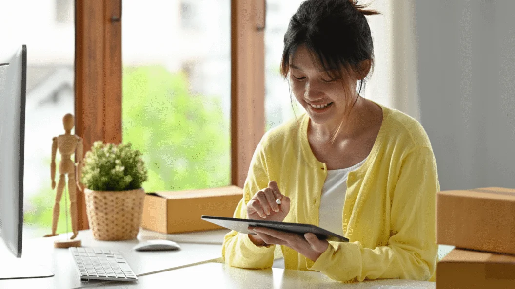 Woman using a tablet at a home office desk with shipping boxes