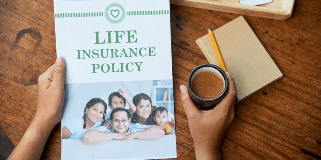 Hands holding a life insurance policy booklet beside a cup of coffee