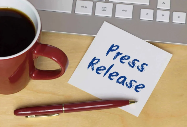 Note reading Press Release beside a coffee mug and pen