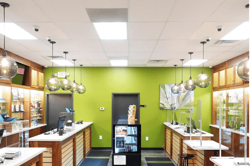 Modern retail store interior with green accent wall, pendant lights, two checkout counters, transparent dividers, and display shelves holding merchandise. Central door and artwork visible on back wall.