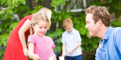 Father helping a child hold a sparkler in a backyard