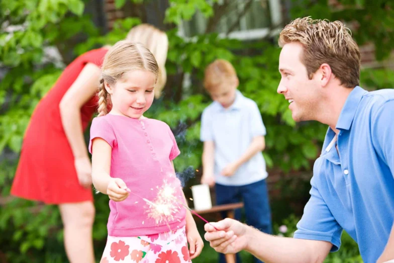 Father helping a child hold a sparkler in a backyard