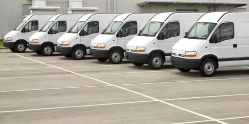 Row of white commercial vans parked outside a warehouse