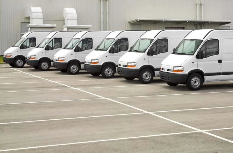 Row of white commercial vans parked outside a warehouse