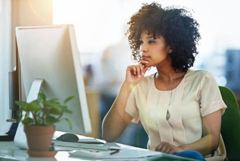 Woman thinking while working at a desktop computer